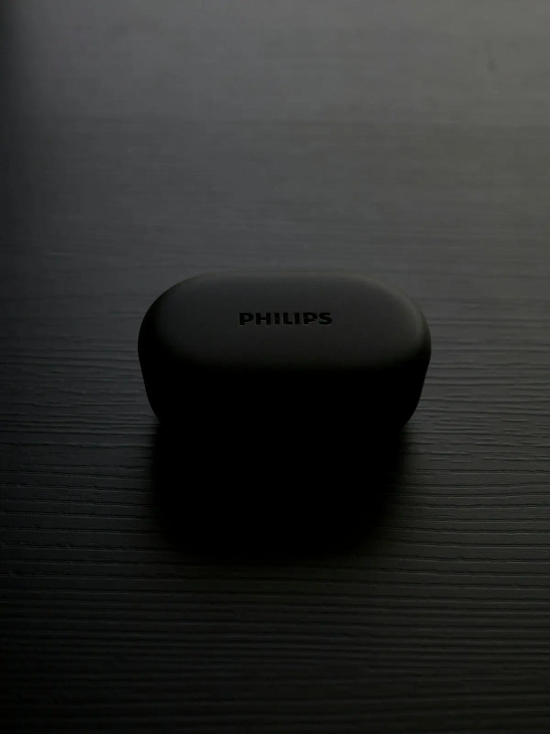 A philips earbuds case sits on a dark surface.